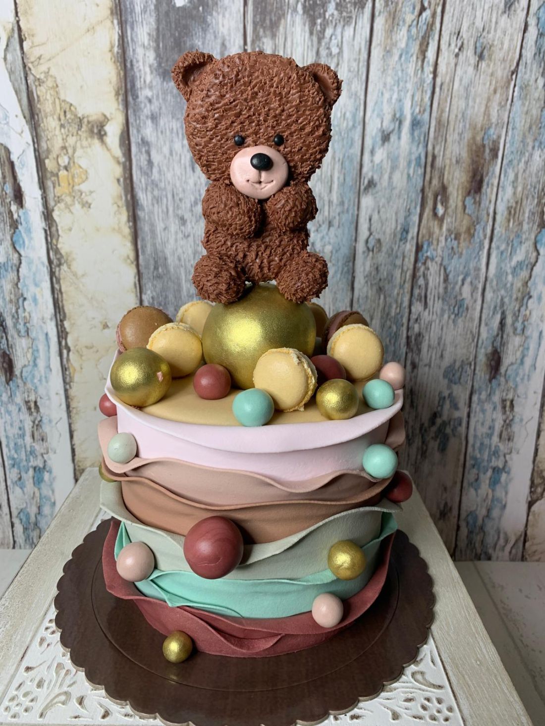Tarta fondant para primer cumpleaños de niña con figura de oso, globo de corazón y bloques de juguete.