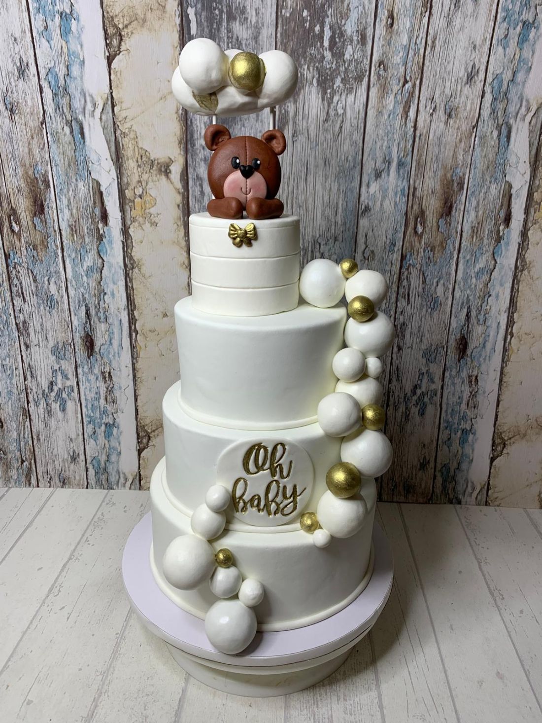 Tarta fondant de baby shower de cuatro pisos en color blanco con oso de peluche